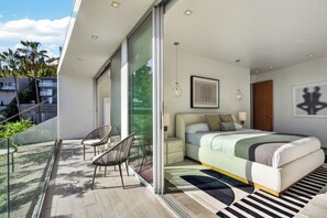 A modern bedroom with a large bed, a glass door leading to a balcony, and a view of the outdoors.