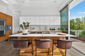 A modern kitchen with a central island, bar stools, and a view of the outdoors.