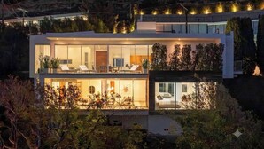 Una casa moderna de dos pisos con un balcón, ventanas amplias y un interior bien iluminado.