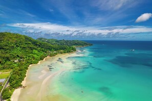 Un paysage côtier avec une plage, des eaux turquoise et limpides, et une végétation luxuriante.
