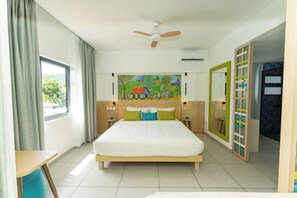 A modern hotel room with a large bed, a ceiling fan, a painting on the wall, and a view of the outdoors through the window.
