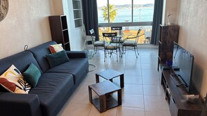 Ein Wohnzimmer mit einem dunkelblauen Sofa, einem Couchtisch, einem Fernseher und einem Essbereich mit Stühlen und einem Tisch.