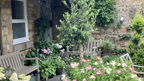 A stone building with a window, a bench, and a variety of potted plants and flowers. - St Lawrence Rest - Cosy Retreat in Warkworth (Morpeth)