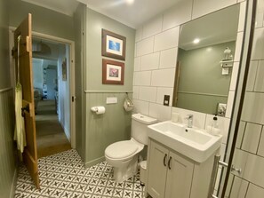 A bathroom with a toilet, sink, and mirror. There are two framed pictures on the wall and a roll of toilet paper on the wall. - St Lawrence Rest - Cosy Retreat in Warkworth (Morpeth)