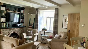 A cozy living room with a fireplace, comfortable seating, a television, and a bookshelf. - St Lawrence Rest - Cosy Retreat in Warkworth (Morpeth)