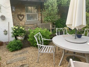 A patio with a round table and white chairs, surrounded by gravel and potted plants. - St Lawrence Rest - Cosy Retreat in Warkworth (Morpeth)