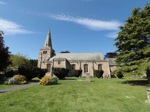 A church with a tall steeple and a clock, surrounded by a well-maintained lawn and trees. - St Lawrence Rest - Cosy Retreat in Warkworth (Morpeth)