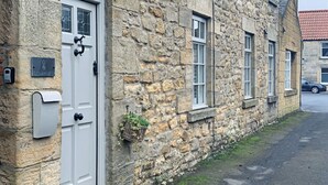 A stone building with a white door, a mailbox, and a small hanging basket. - St Lawrence Rest - Cosy Retreat in Warkworth (Morpeth)
