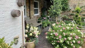 A stone building with a white exterior, a wooden bench, and potted plants with flowers. - St Lawrence Rest - Cosy Retreat in Warkworth (Morpeth)