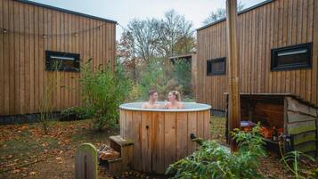 Una cabaña de madera con un jacuzzi en el centro, rodeada de árboles y una terraza de madera.