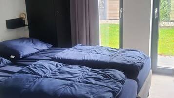 Un dormitorio con dos camas, un cabecero oscuro y un ventanal corredero que da a un balcón.