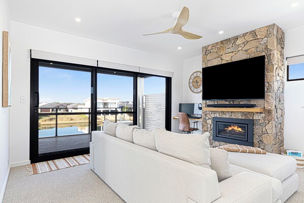 A modern living room with a stone fireplace, a large flat-screen TV, and a sofa. - Ultimate luxury on the canal (Geographe)