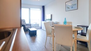 Una cocina moderna con un lavamanos, un comedor con una mesa redonda y sillas, un sofá y un amplio ventanal con vistas al exterior.