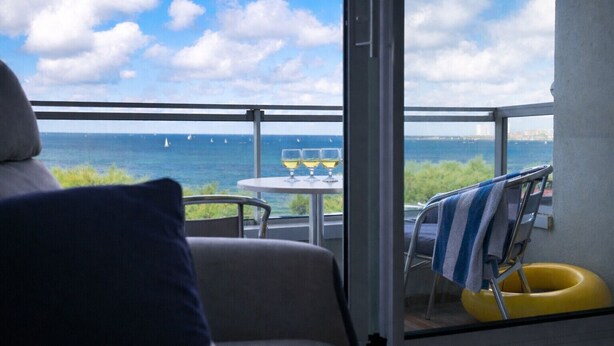 Un balcón con vista al mar, una mesa con vasos y una silla con una toalla.