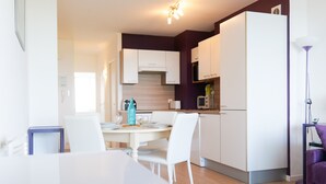Una cocina moderna con armarios blancos, una mesa de comedor con sillas y un refrigerador.