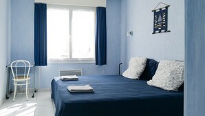 Un dormitorio con cama, dos almohadas, una silla, una ventana con cortinas y un adorno en la pared.