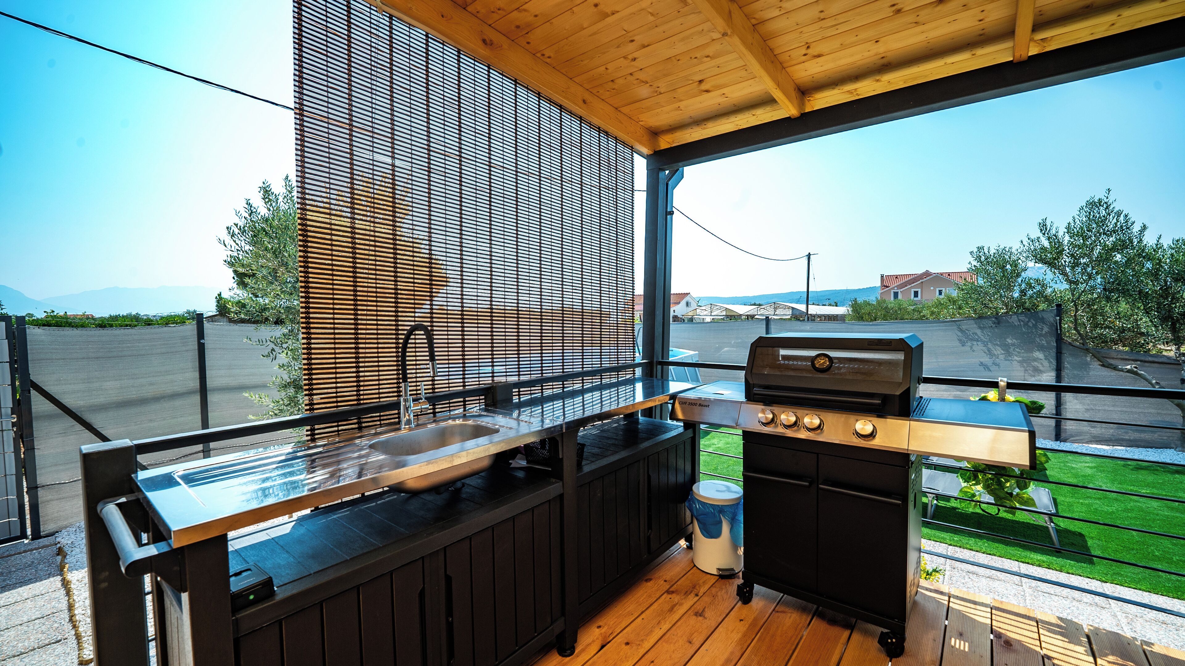 An outdoor kitchen with a grill, sink, and wooden deck.
