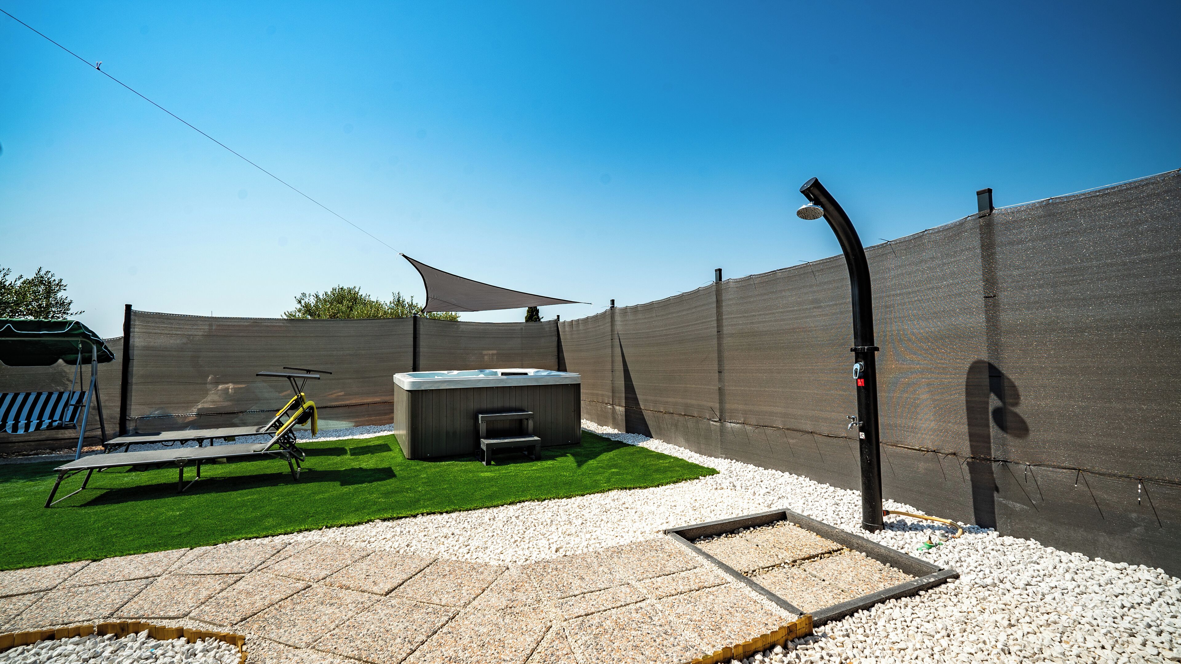 Un patio trasero con jacuzzi, un trampolín y una zona de patio con una pérgola.