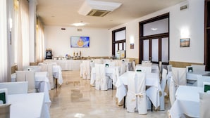 Un salón de banquetes con filas de mesas dispuestas para un evento formal, una zona de bufé y un cuadro grande en la pared.