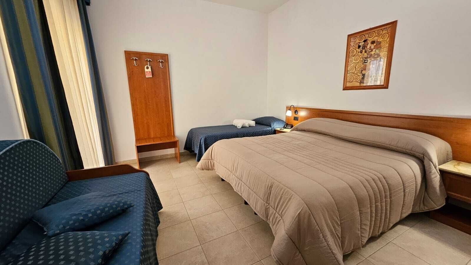 Ein Hotelzimmer mit einem großen Bett, einem kleineren Bett, einer Couch, einem Holzschrank und einem Bild an der Wand.
