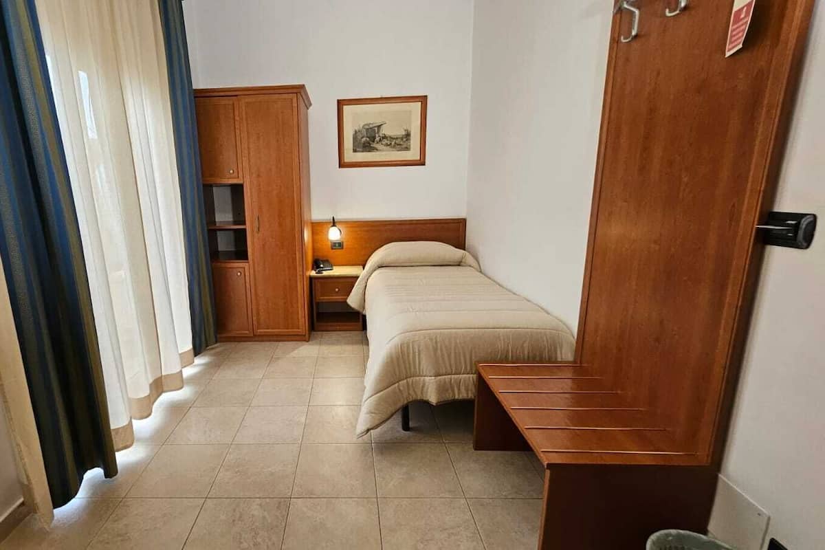 A hotel room with a bed, a desk, a wardrobe, and a nightstand.