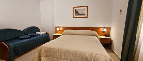 A hotel room with a bed, a sofa, two bedside tables with lamps, and a framed picture on the wall.