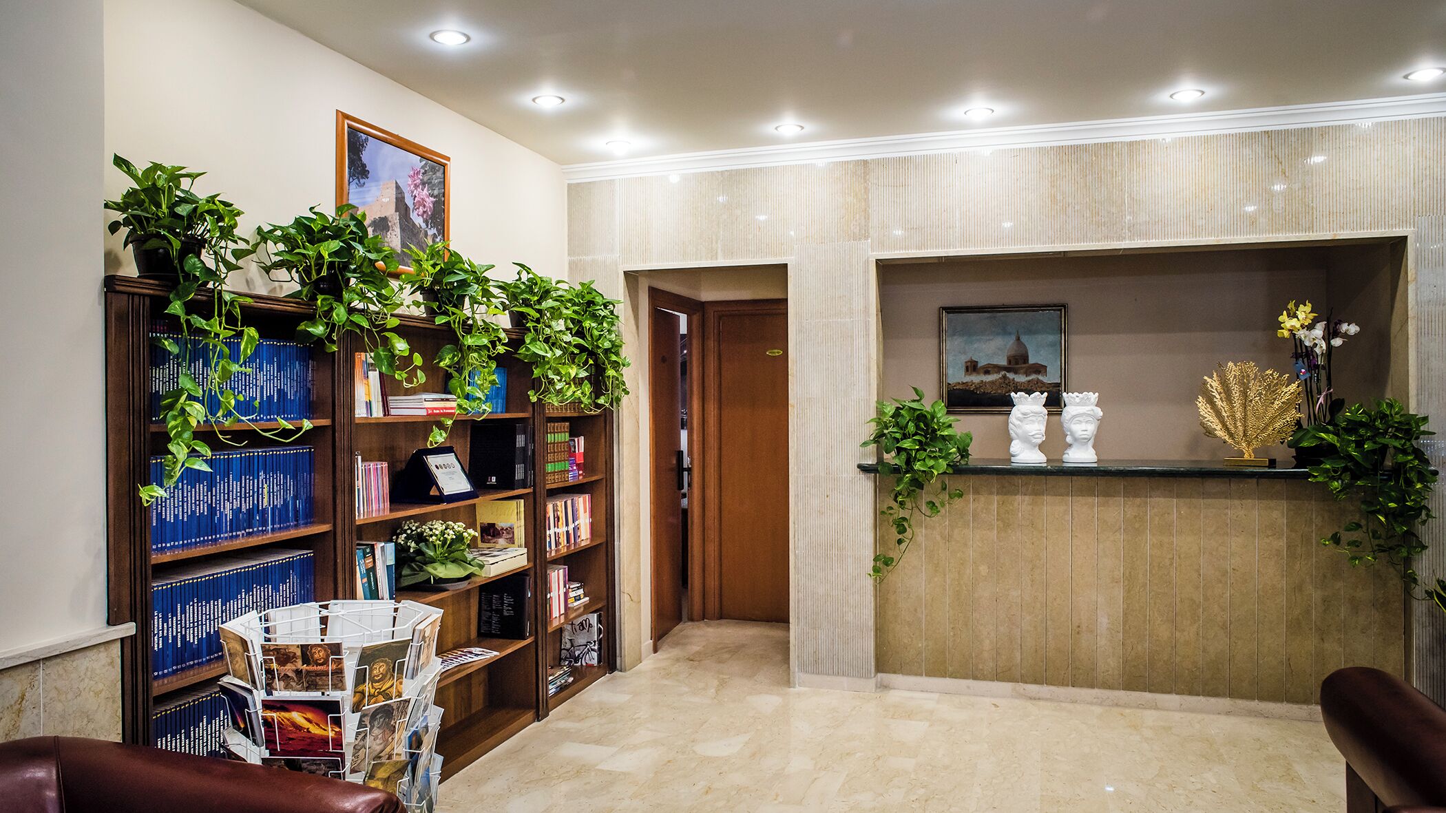 Un área de recepción con suelo de mármol, un mostrador de madera, una estantería llena de libros y una planta en maceta.