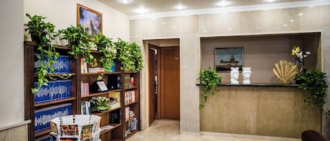 Un área de recepción con suelo de mármol, un mostrador de madera, una estantería llena de libros y una planta en maceta.
