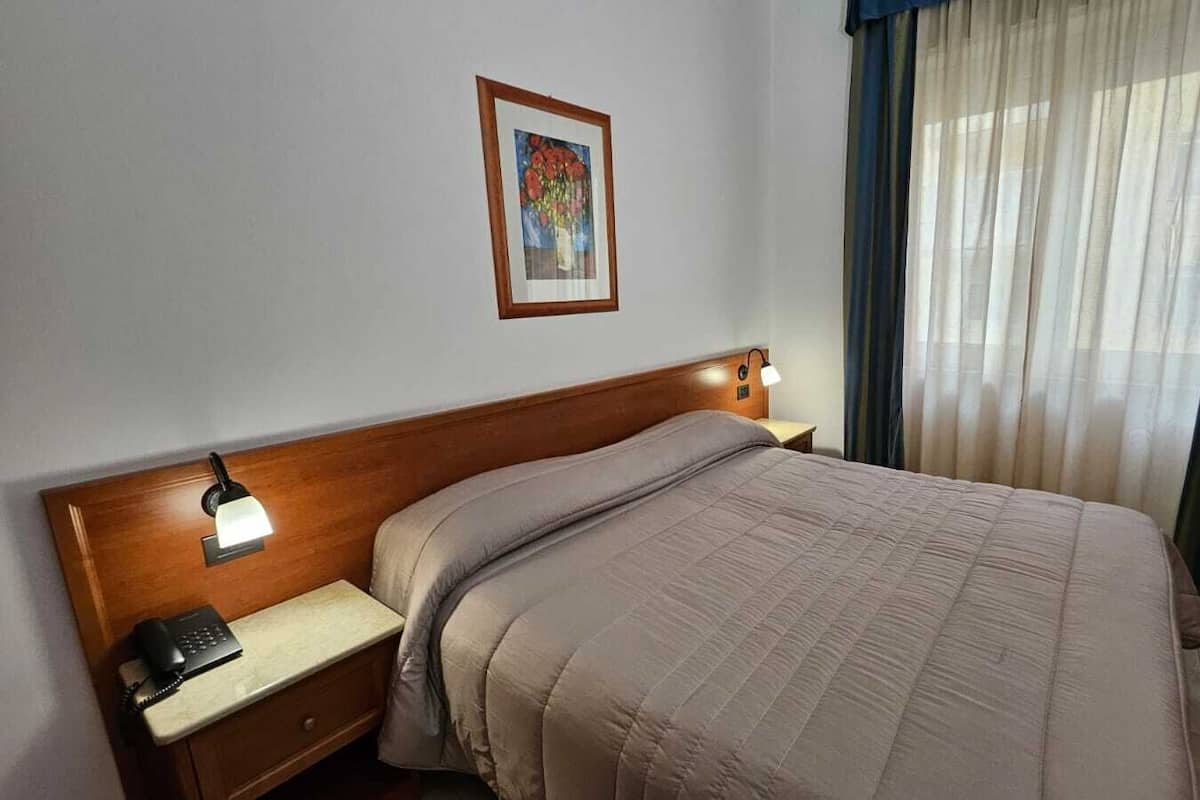 A hotel room with a large bed, wooden headboard, bedside lamps, a telephone, and a painting on the wall.