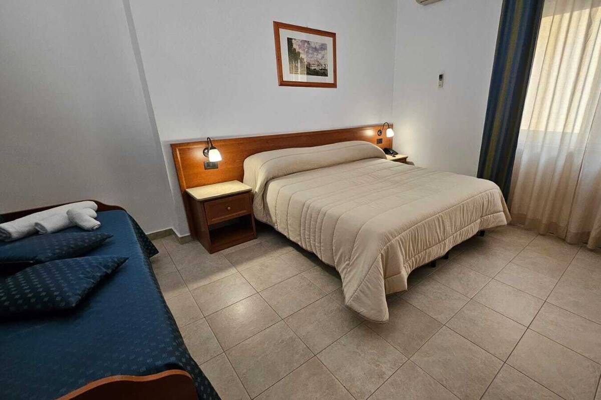 A hotel room with a bed, a smaller bed, a nightstand, a lamp, and a picture on the wall.