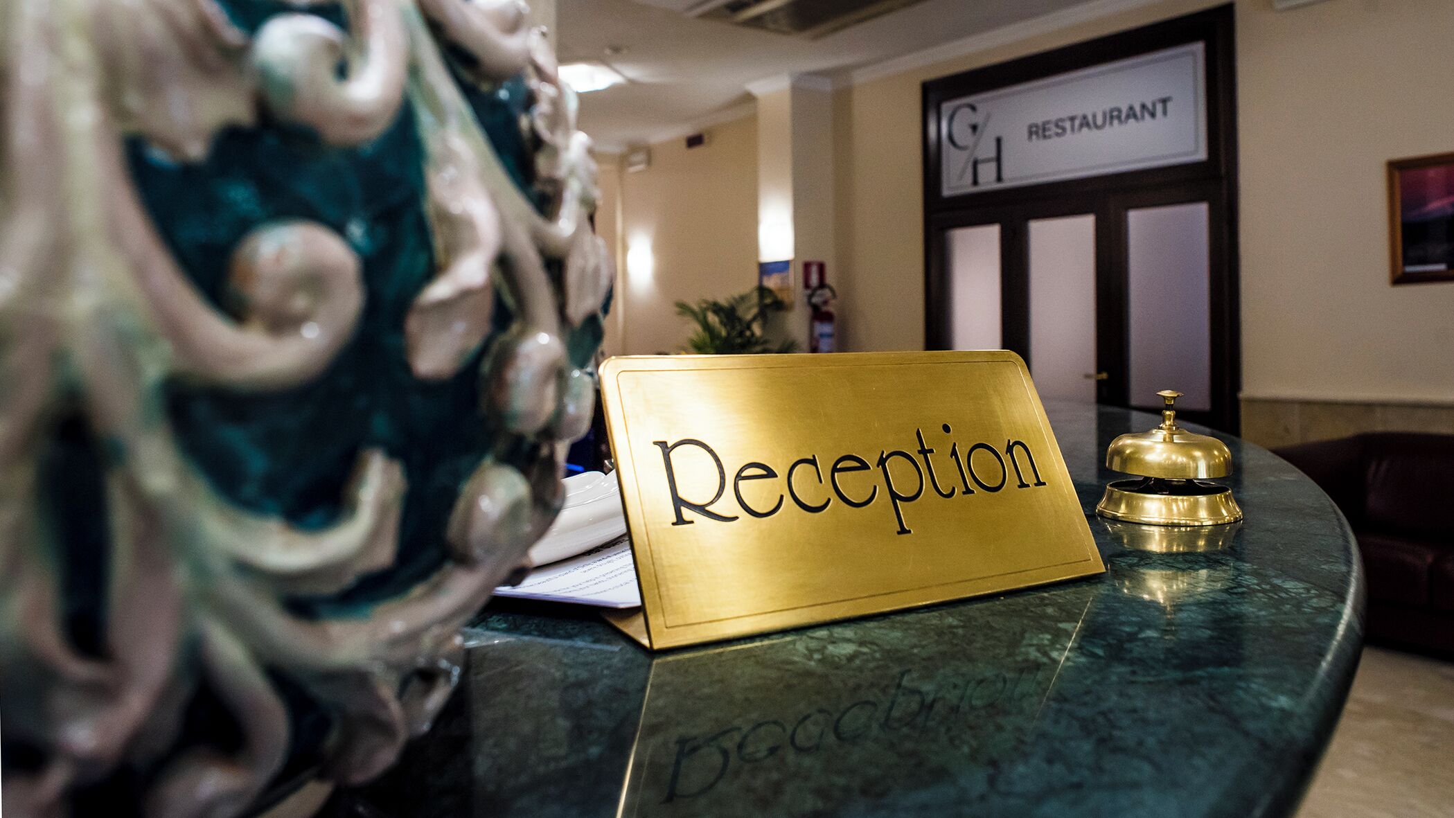 A reception desk with a 'Reception' sign, a gold bell, and a decorative vase.
