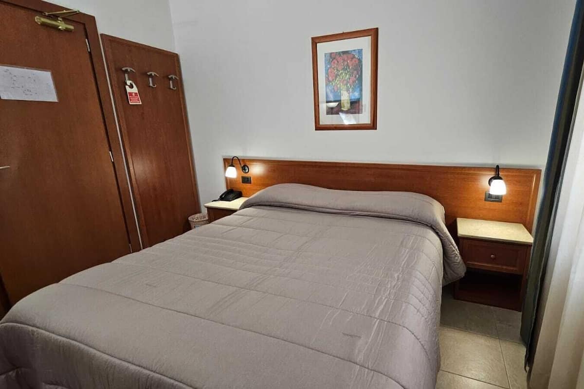 A hotel room with a bed, a nightstand, a desk, and a wardrobe.
