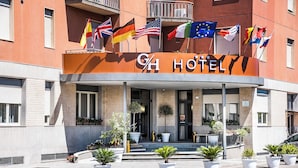 Un hotel con fachada moderna, varias banderas y una entrada acogedora con plantas en macetas.