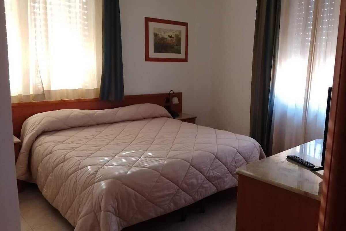 A bedroom with a bed, a nightstand, a desk, and a door.