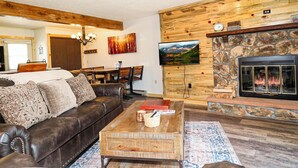 Una sala de estar acogedora con chimenea de piedra, un sofá de cuero y un televisor montado en la pared.