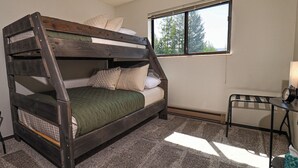 Una cama individual superpuesta con ventana, una mesita y una silla en una habitación con suelo alfombrado.