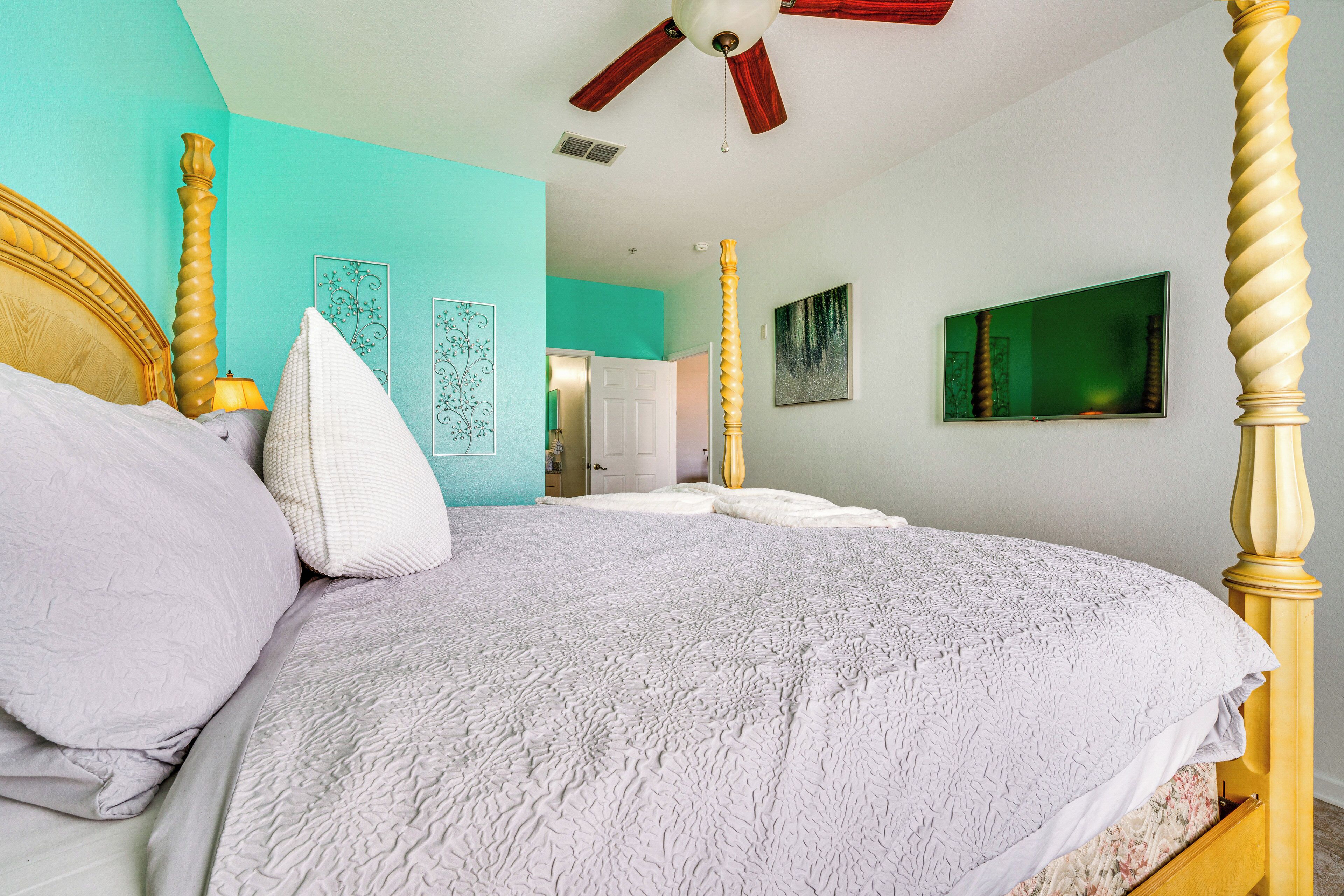 A bedroom with a four-poster bed, a ceiling fan, and artwork on the walls.