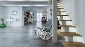 Un vaste espace de vie comprenant un canapé blanc moderne, une table à manger avec des chaises et un escalier avec des marches en bois.