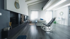 Un salon moderne avec une cheminée, un canapé blanc, un fauteuil à bascule et un coin repas comprenant une table et des chaises blanches.