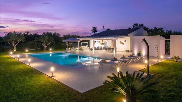 Une maison moderne dotée d’une piscine, d’un espace salon extérieur et d’un patio bien éclairé.