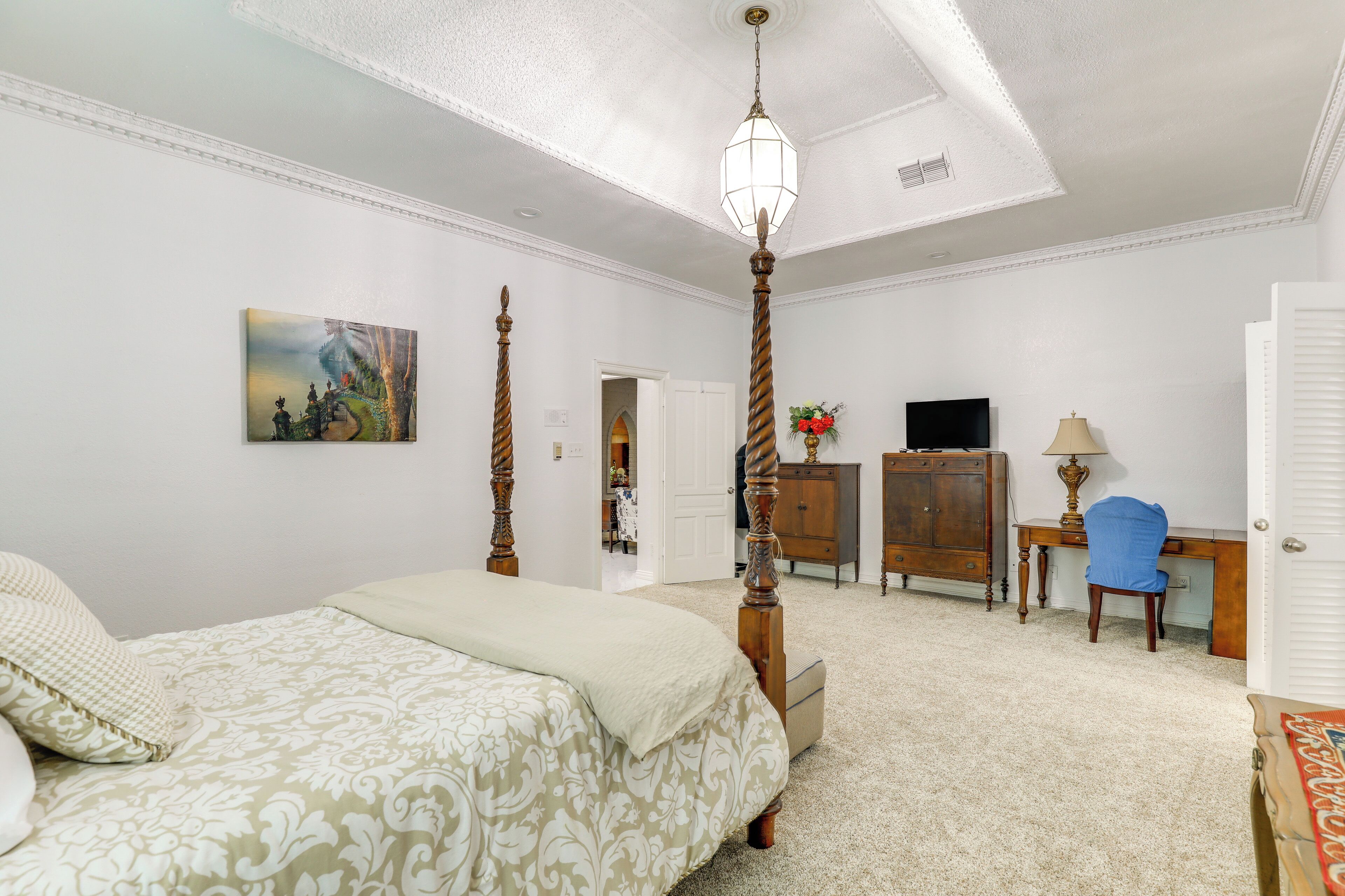 A bedroom with a four-poster bed, a desk, a chair, and a television.