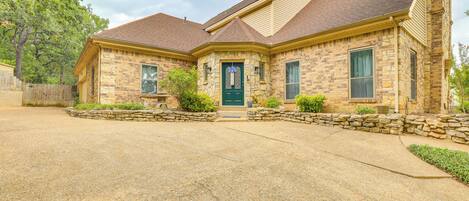 A two-story stone house with a green front door, stone steps, and a stone wall surrounding the driveway.