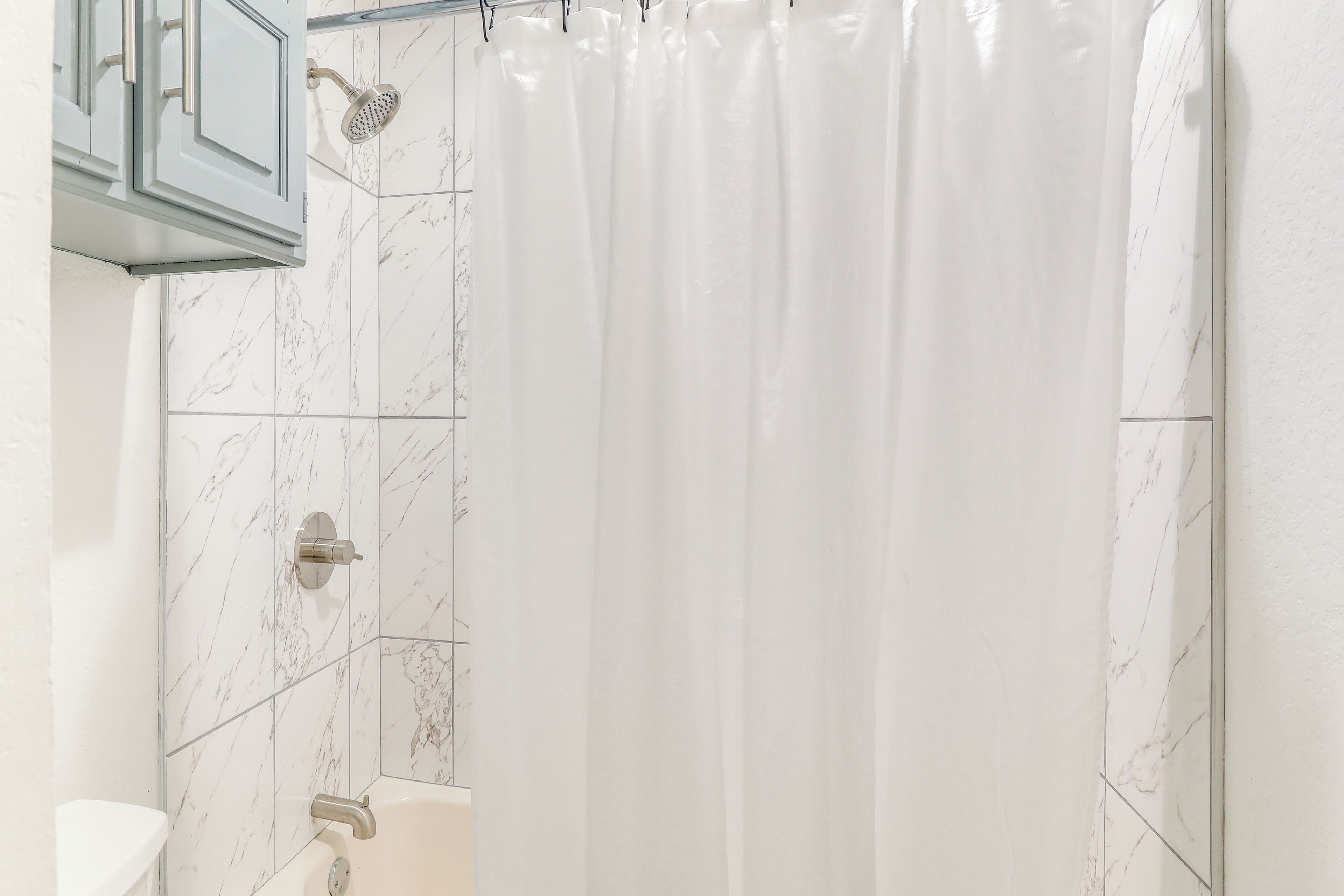 A bathroom with a shower, toilet, and marble tiles.