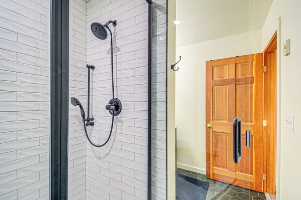 A shower with a glass enclosure, a wooden door, and a tiled floor.