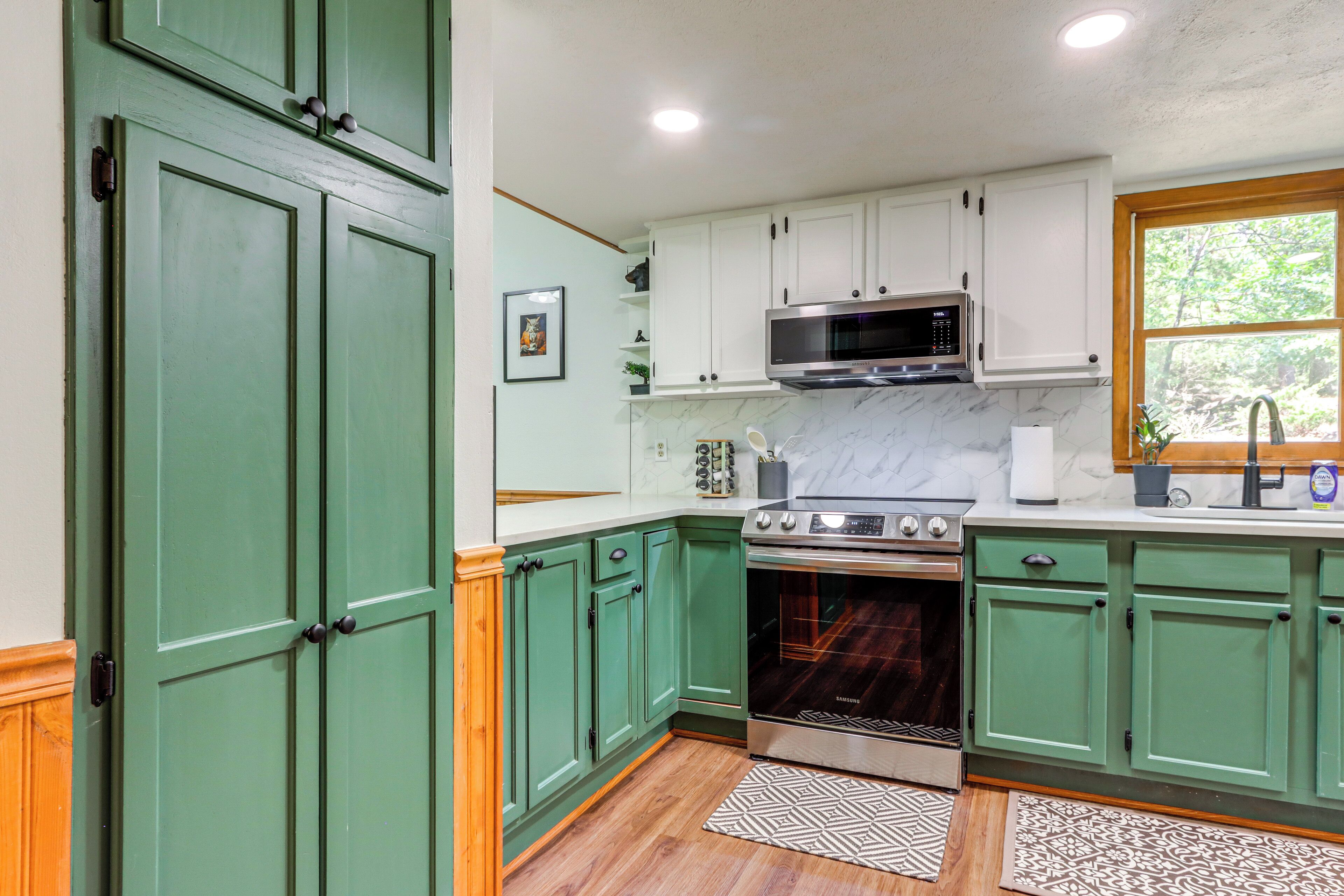 A kitchen with green cabinets, a microwave, stove, and marble backsplash.