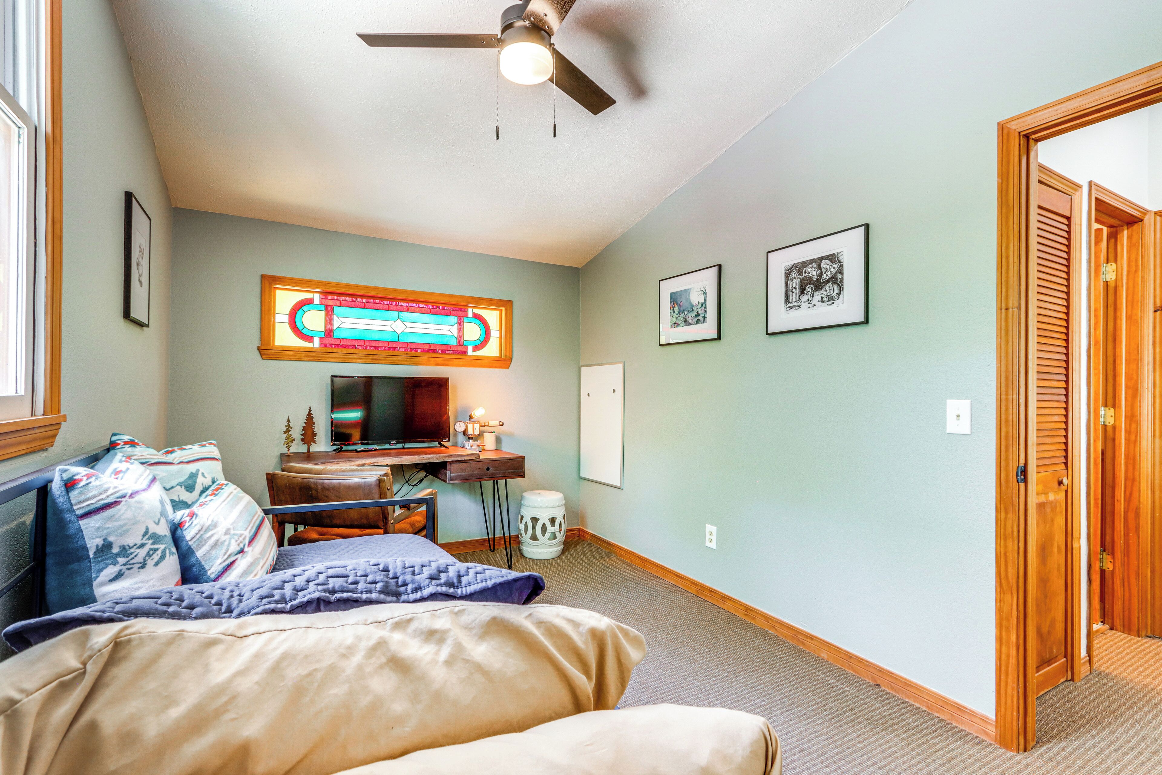 Une chambre à coucher comprenant un lit, un bureau, un ventilateur de plafond et un luminaire fixé au mur.