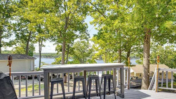 A wooden deck with a railing, three barstools, and a table.