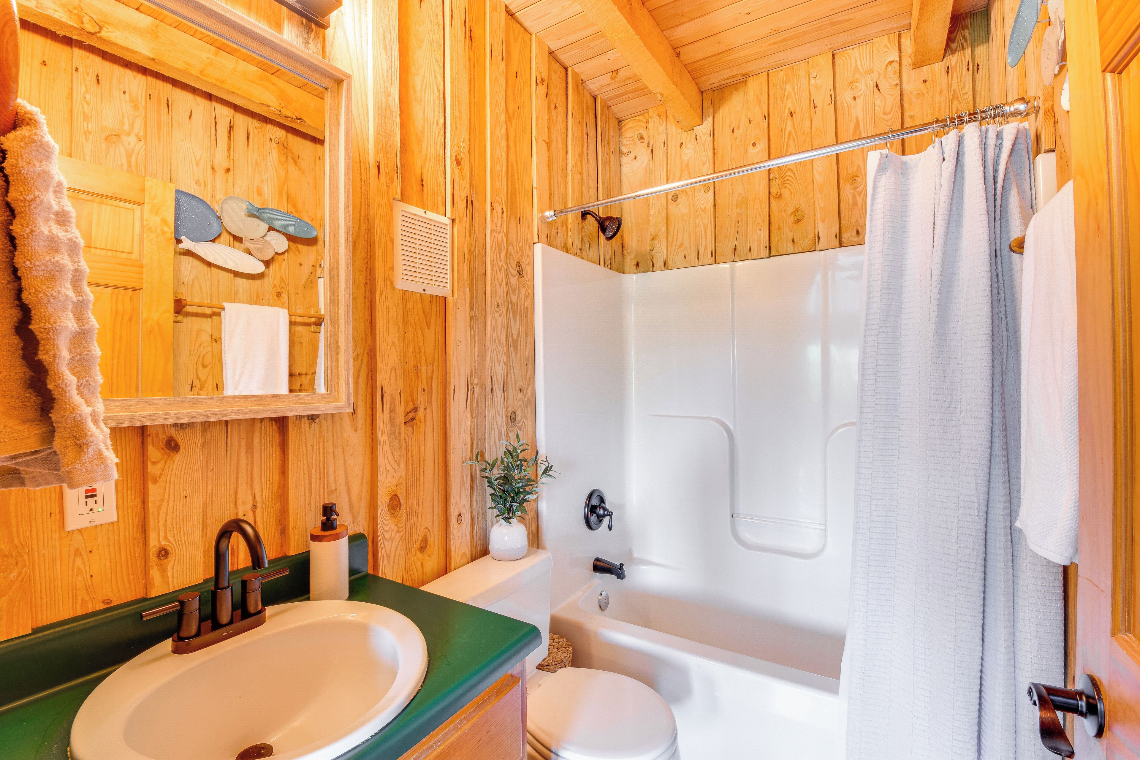 Une salle de bain rustique, avec des murs en bois, comprenant un lavabo, des toilettes et une baignoire.