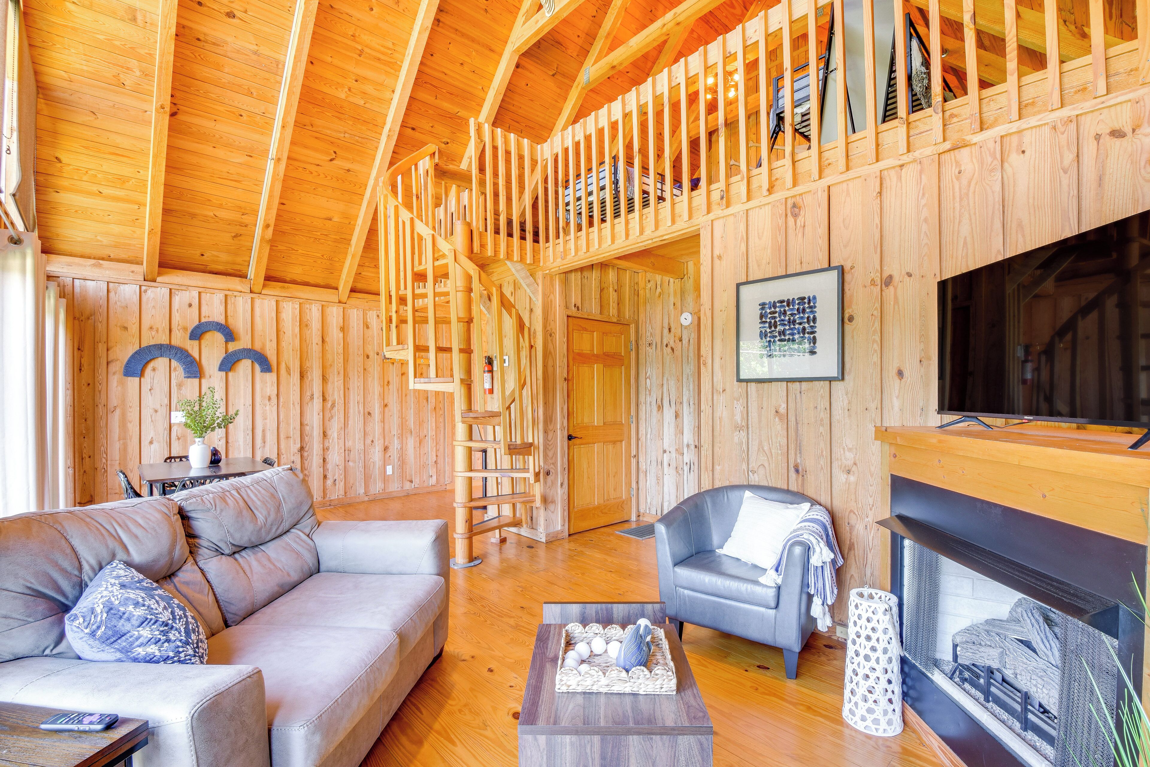 A wooden interior with a sofa, armchair, fireplace, and wooden staircase.