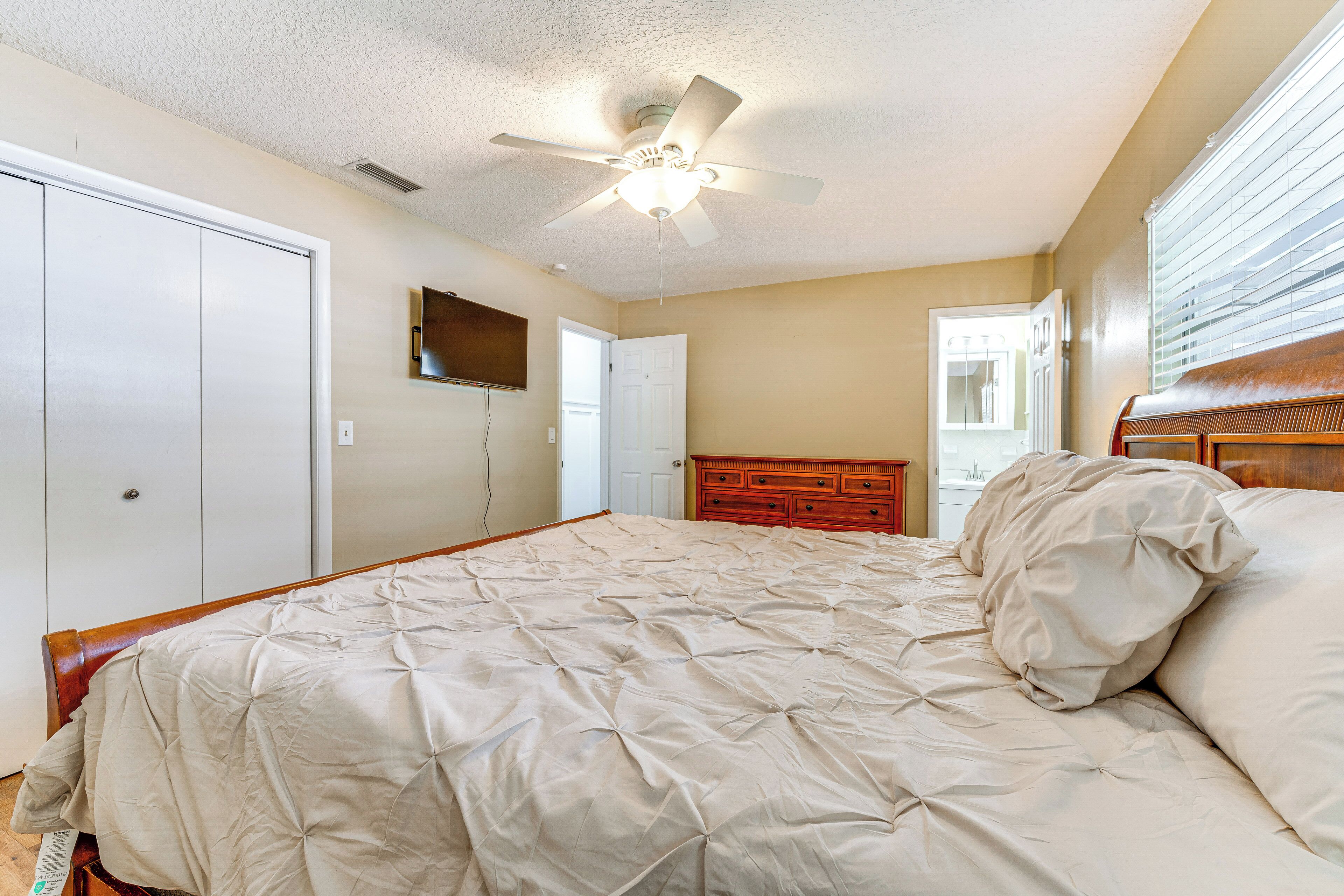 A bedroom with a large bed, a wooden dresser, a ceiling fan, and a door.